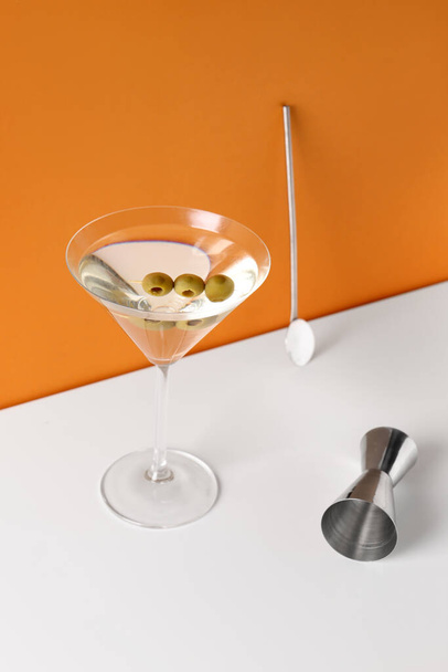 Glass of martini with olives, bar spoon and jigger on color background - Foto, Imagem