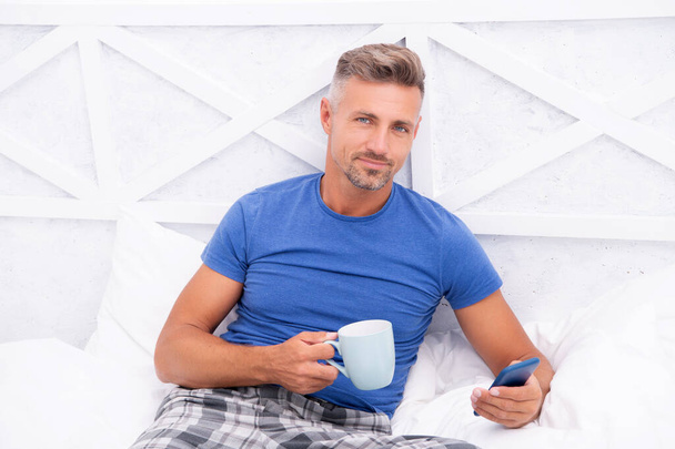 cheerful man messaging in morning in bedroom. man messaging in morning at home. man messaging in morning. man messaging in morning in bed. - Photo, image