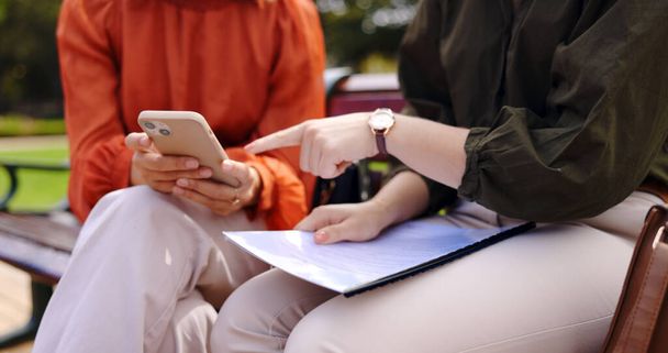 Business, closeup and women on a bench, smartphone or planning for collaboration, documents or discussion. Female professionals, freelancers or partners in a park, cellphone or mobile app for project. - Foto, imagen