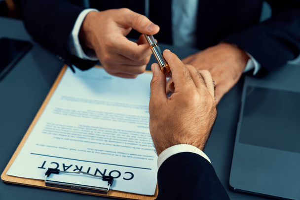 Two businesspeople sit across the desk as business deal is taking place. Corporate attorney giving a pen for client or partner to sign contract paper, sealing the deal with signature. Fervent - 写真・画像