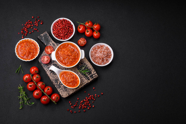 Délicieuse sauce tomate épicée au poivre, ail, sel, épices et herbes dans un bateau à sauce blanche sur fond de béton foncé - Photo, image