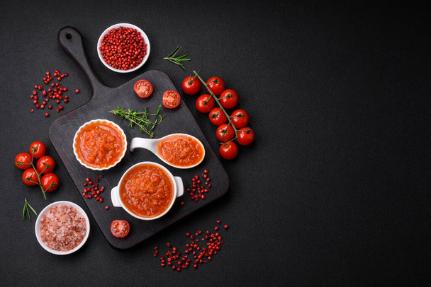 Délicieuse sauce tomate épicée au poivre, ail, sel, épices et herbes dans un bateau à sauce blanche sur fond de béton foncé - Photo, image