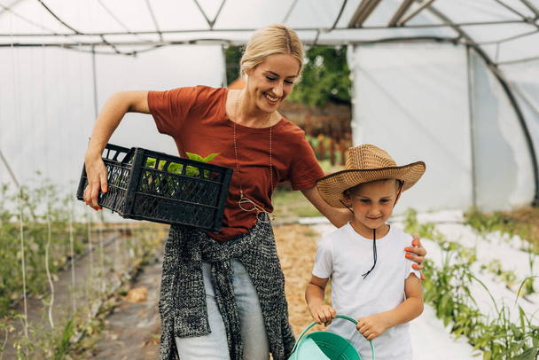 Loving mother and her son are working together in the greenhouse. - Zdjęcie, obraz