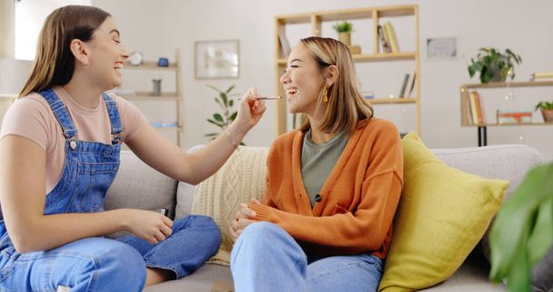 Women friends, makeup and lipstick while happy on home sofa and talking about product on lips. Females or sisters relax on living room couch for funny conversation about cosmetics and beauty. - Photo, Image