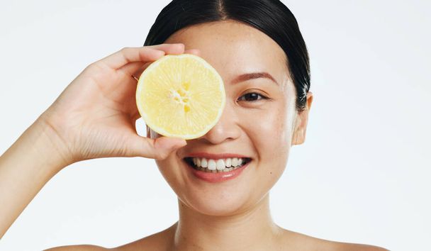 Lemon, face and woman in studio, natural wellness and white background. Happy asian model, beauty portrait and citrus fruits for facial cosmetics glow, vitamin c skincare or detox dermatology results. - Foto, immagini