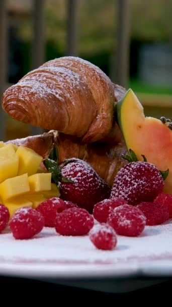 果実のある暗い背景では、焼きたてのクロワッサンとトレイにフルーツと、コーヒーとの珍しい創造的な朝食。コンセプト:おはよう、朝食、おいしい、スローモーション、果物. - 映像、動画