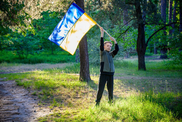 Ουκρανό αγόρι με κυματιστή σημαία και προσεύχεται να σταματήσει τον πόλεμο στην Ουκρανία σε ένα πεδίο στο ηλιοβασίλεμα. Πόλεμος της Ρωσίας εναντίον της Ουκρανίας. Σταματήστε τον πόλεμο. - Φωτογραφία, εικόνα
