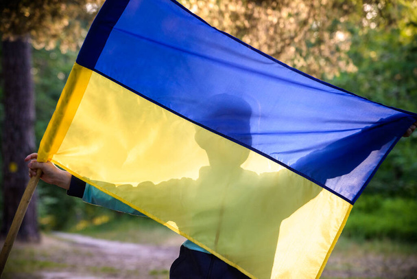旗を振って、日没時にフィールドでウクライナでの戦争を停止するために祈るとウクライナの少年。ロシアとウクライナの戦争。戦争を止める. - 写真・画像