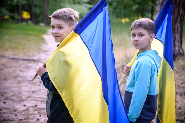 σημαίες της Ουκρανίας στα χέρια δύο αγοριών. Τα παιδιά κρατούν Ουκρανικές σημαίες κίτρινες και μπλε κυματίζουν στον άνεμο. Ημέρα Ανεξαρτησίας της Ουκρανίας. Ημέρα σημαίας. - Φωτογραφία, εικόνα