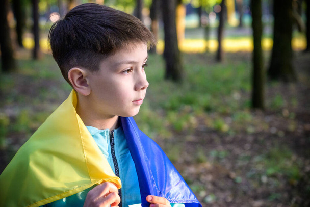 心配10代の愛国者は肩に青い黄色のウクライナ国旗をつけている。春の自然背景。ウクライナのシンボル。愛国心. - 写真・画像