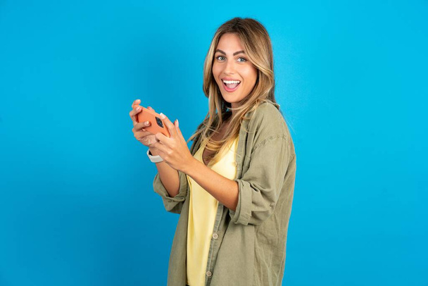 Szép addicted vidám szép szőke nő visel overshirt a kék háttér segítségével szerkentyű játék hálózati játék - Fotó, kép
