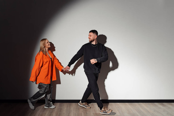 Corpo inteiro de homem feliz levando sua namorada pela mão em quarto escuro iluminado por holofotes - Foto, Imagem