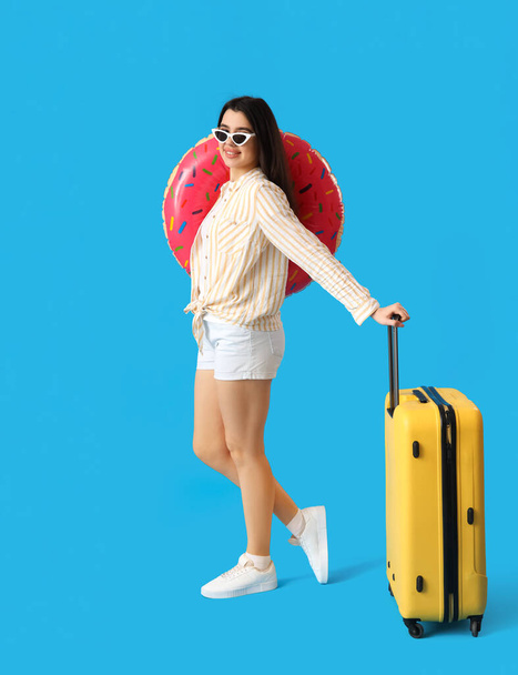 Young woman with inflatable ring and suitcase on blue background - Foto, Imagem