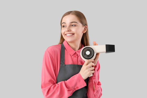 Female hairdresser with dryer on grey background - Фото, изображение