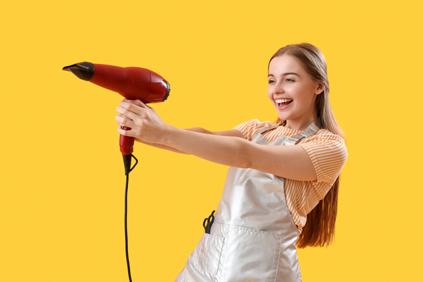 Female hairdresser with dryer on yellow background - Zdjęcie, obraz