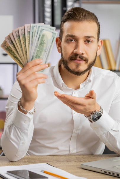 Young boss business man showing money dollar cash gives to you wages salary, satisfied with good work. Success, wealth, investment. Freelancer guy at office workplace looking at camera. Vertical shot - Foto, Imagen