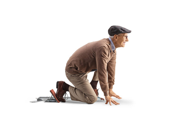 Full length profile shot of an elderly man kneeling on starting blocks isolated on white background - Foto, Bild