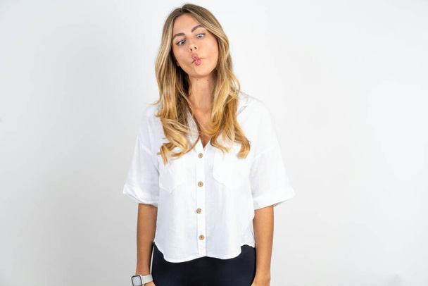 Young caucasian businesswoman wearing white shirt over white background making fish face with lips, crazy and comical gesture. Funny expression. - Photo, Image