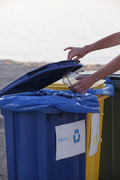Woman hand throwing plastic glass into recycling bin. Concept of protecting the environment by reducing air and water pollution and saving energy - Photo, Image