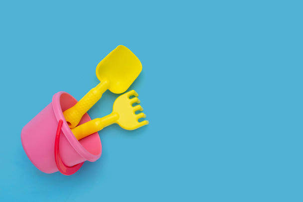 Plastic toys, shovels in bucket on blue background. Summer background concept - Photo, Image