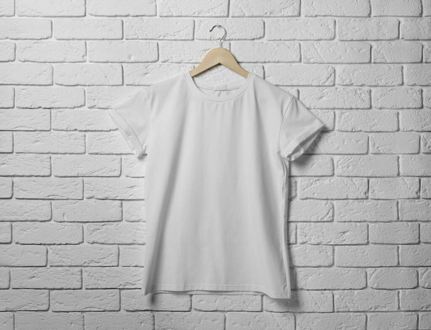 Hanger with stylish T-shirt on white brick wall - Zdjęcie, obraz