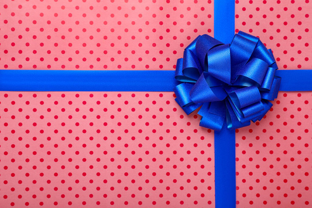 Blue ribbons with bow on red polka dot wrapping paper, top view - Foto, imagen