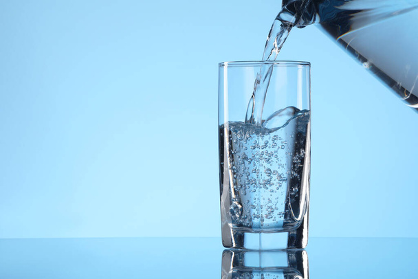 Pouring water from jug into glass on light blue background. Space for text - Photo, Image