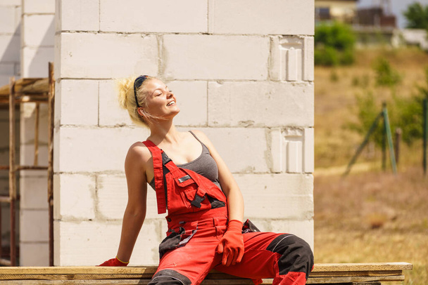 Woman in dungarees relaxing after hard work on construction site. Young female lying outdoor taking a break - Foto, Imagen