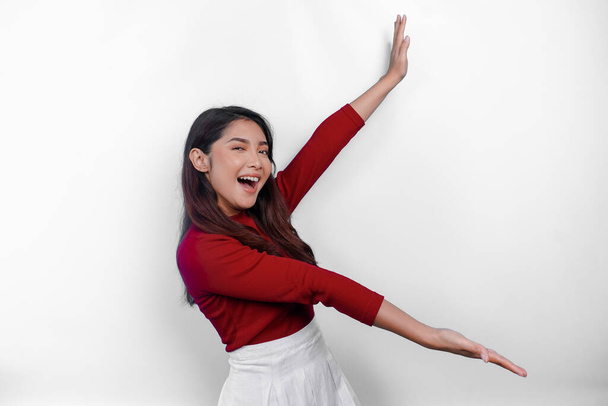 Excited Asian woman wearing red t-shirt, pointing at the copy space beside her, isolated by white background - Foto, afbeelding