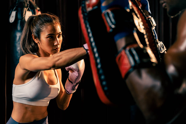 Azjatka Muay Thai bokser uderza w zaciętej sesji treningu bokserskiego, dostarczając strajk do jej sparing trener noszenie rękawic bokserskich, pokazując Muay Thai techniki bokserskiej i umiejętności. Impetus - Zdjęcie, obraz
