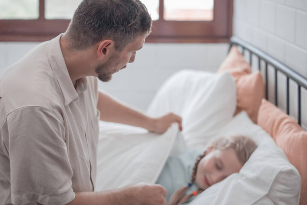 Father singing his daughter to sleep, providing comfort, support, and security. Focusing on fulfilling both physical and emotional needs. Kids sometimes act happy while pretending to fall asleep. - Фото, изображение