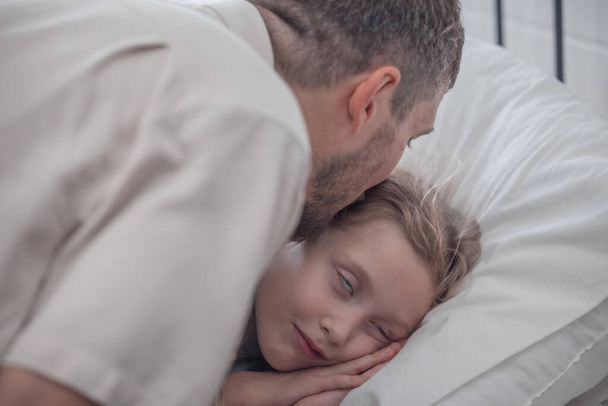 Father singing his daughter to sleep, providing comfort, support, and security. Focusing on fulfilling both physical and emotional needs. Kids sometimes act happy while pretending to fall asleep. - Photo, image