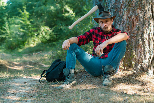 Handsome man lumberjack with a large ax examines the tree before felling. Deforestation is a major cause of land degradation and destabilization of natural ecosystems - Photo, image