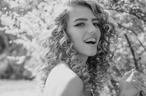 Smiling spring curly girl. Sensual blonde in Blooming flowers in orchard. Spring day concept. Good day - Photo, Image