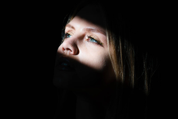 Portrait of elegant woman with light on a black background. Beautiful female face in the darkness - Fotografie, Obrázek