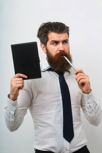 Portrait with copy space of serious bearded man holding copybook and with pen with thoughtful expression over white background - Fotó, kép