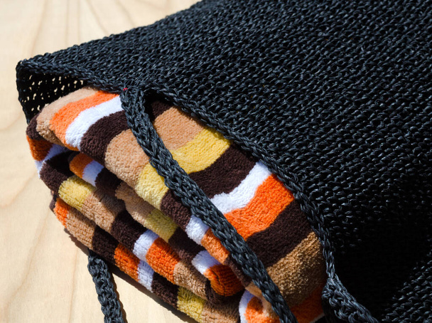 Bolso de rafia negro y toalla de colores sobre un fondo de madera. Bolso hecho a mano para mujer. - Foto, imagen