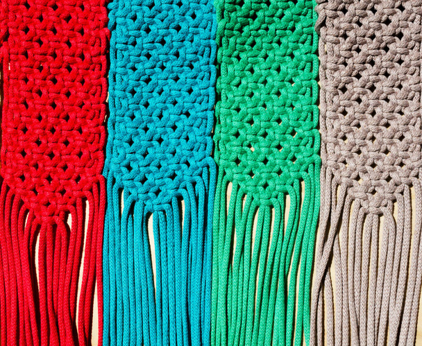 Macrame-Technik, ein quadratischer Knoten aus mehrfarbigen Fäden. Farbige Makramabänder in den Farben blau, gelb, rot, beige, grün und rosa. - Foto, Bild
