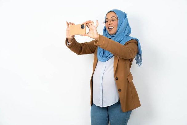 mujer musulmana embarazada usando hijab tomando una selfie para publicarla en las redes sociales o tener una videollamada con amigos. - Foto, imagen