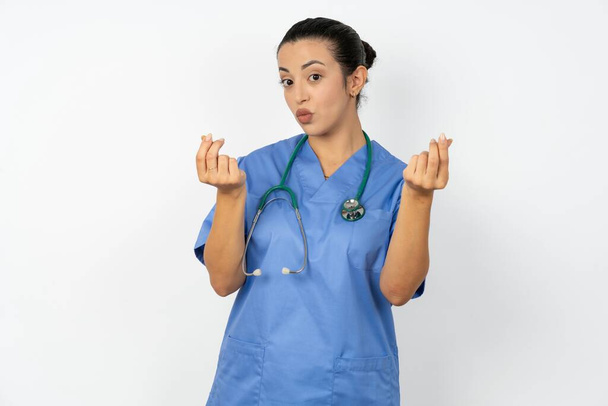 Arap doktor kadın mavi üniforma giyiyor. Elleriyle jest yapıyor. Maaş istiyor. - Fotoğraf, Görsel