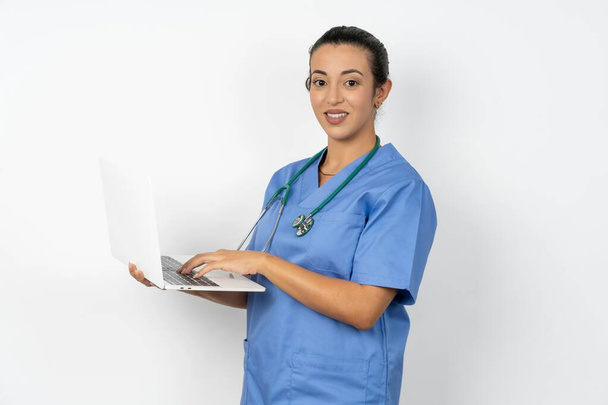 Imádnivaló arab orvos nő visel kék egyenruhát gazdaság laptop - Fotó, kép