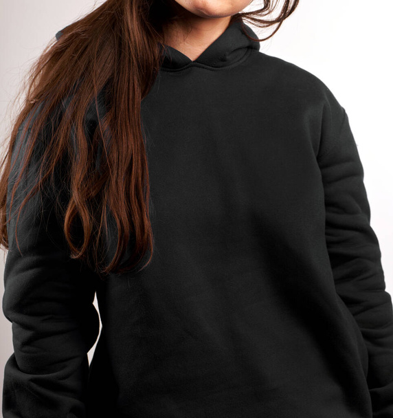 Μια γυναίκα φοράει μαύρη κουκούλα. Το εμπορικό σήμα των ρούχων του δρόμου. Λογότυπο στο πρότυπο πουκάμισο αντίγραφο χώρου. - Φωτογραφία, εικόνα