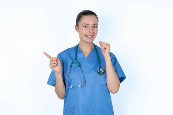 blank vrouw arts in uniform met stethoscoop punten op lege ruimte houden vuist omhoog, winnaar gebaar. - Foto, afbeelding