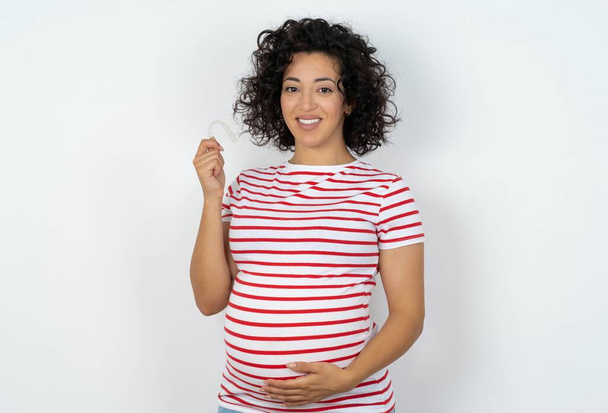 Беременная женщина, держащая невидимые скобки, выравнивает, рекомендуя это новое лечение. Концепция стоматологии. - Фото, изображение