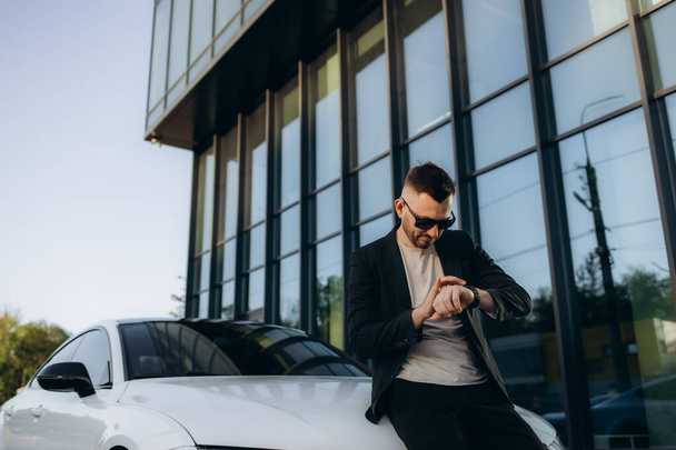 Чоловік, який чекає на клієнта, чоловік-покупець у сірому костюмі, обирає автомобільний погляд на час розумний годинник хоче купити новий автомобіль у автосалоні дилерський магазин автосалон концепція продажу
 - Фото, зображення