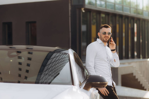 Biznesmen rozmawiający przez smartfon stojący w pobliżu samochodu. - Zdjęcie, obraz