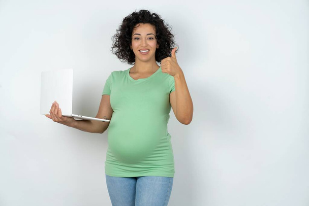 Gyönyörű vonzó terhes nő tartja netbook és mutatja hüvelykujját fel - Fotó, kép