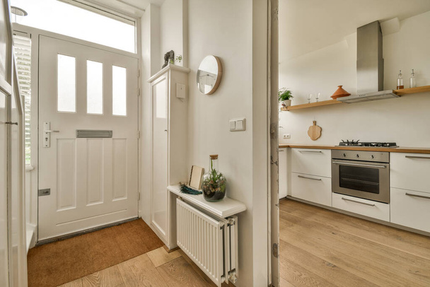 egy fehér konyha fapadlóval és egy nyitott ajtó vezet a nappaliba a másik oldalon - Fotó, kép