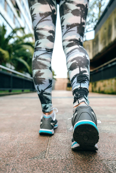 Gros plan de jeunes femmes méconnaissables jambes prêtes à courir portant des baskets et des leggings tropicaux avec des palmiers - Photo, image