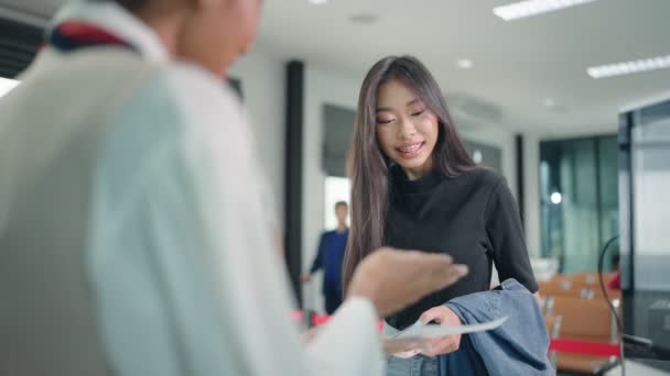 Onnellinen aasialainen nainen matkustaja antaa lennolle kulkulupa ja passi asiakkaan check in upseeri palvelutiskillä lentokentällä - Materiaali, video
